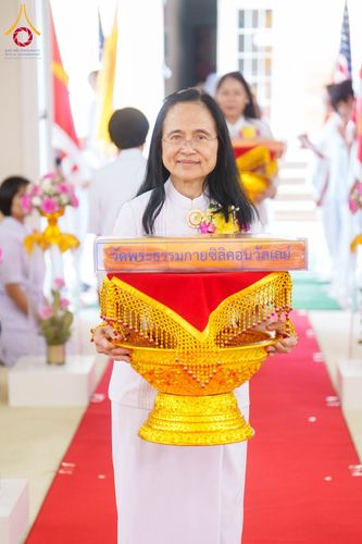 หญิงไทยสวมชุดขาวถือพานพุ่มสีทองที่มีผ้าไตรวางอยู่ด้านบนในพิธีทางศาสนา