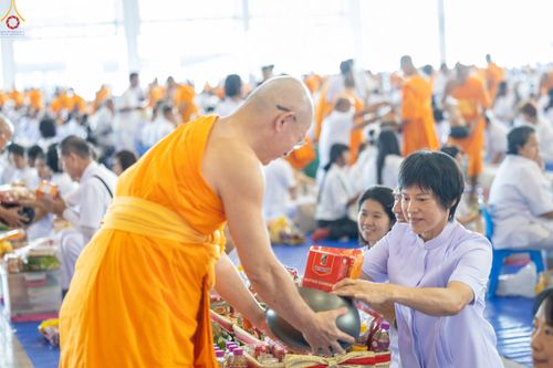 พุทธศาสนิกชนสวมชุดขาวกำลังถวายสิ่งของใส่บาตรแด่พระภิกษุสงฆ์ในพิธีตักบาตร