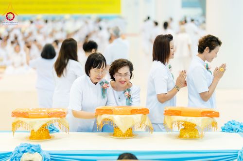 กลุ่มผู้หญิงในชุดสีขาวกำลังประกอบพิธีทอดผ้าป่าโดยมีพานวางผ้าไตรสีเหลืองทองวางอยู่บนโต๊ะ