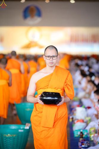 พระภิกษุสวมแว่นตาถือบาตรสีดำในพิธีตักบาตร