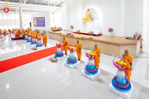 พระภิกษุสงฆ์ห่มจีวรสีส้มกำลังประกอบพิธีบรรจุพระบรมสารีริกธาตุลงในเกศดอกบัวตูมจำลองภายในอาคาร
