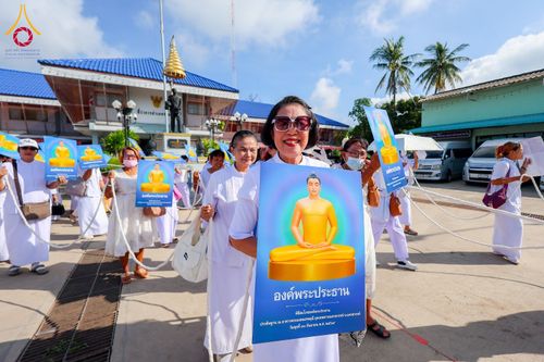 กลุ่มคนสวมชุดขาวถือป้ายภาพพระพุทธรูปสีทองเดินขบวนกลางแจ้ง