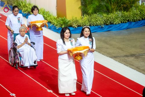 กลุ่มคนในชุดขาวเดินบนพรมแดงอัญเชิญผ้าไตรในพิธีทางศาสนา