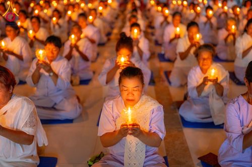 กลุ่มผู้เข้าร่วมโครงการอบรมอุบาสิกาแก้วสวมชุดสีขาวนั่งสมาธิถือเทียนสว่างไสวในพิธีกรรมทางศาสนา