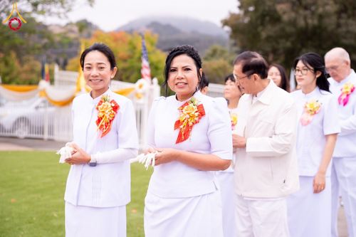 กลุ่มคนสวมชุดสีขาวติดดอกไม้ประดับที่หน้าอกกำลังเดินแถวร่วมพิธีทางศาสนา