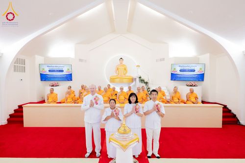กลุ่มพระภิกษุสงฆ์และพุทธศาสนิกชนในชุดขาวร่วมพิธีทางศาสนาหน้าพระพุทธรูปภายในวัด