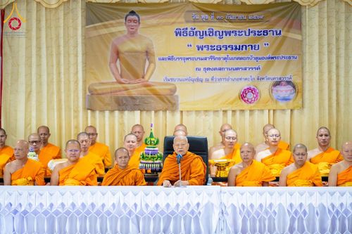 คณะสงฆ์นั่งบนเวทีในพิธีทางศาสนา ด้านหลังมีป้ายไวนิลระบุชื่อพิธีอัญเชิญพระประธานและบรรจุพระบรมสารีริกธาตุ