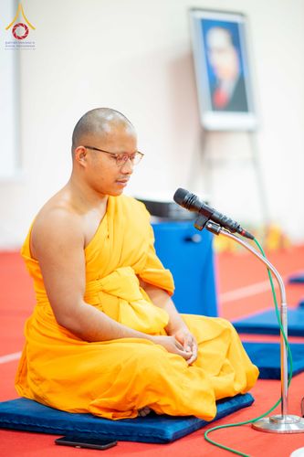 พระภิกษุสงฆ์นั่งสมาธิบนอาสนะสีน้ำเงินโดยมีไมโครโฟนตั้งอยู่ด้านหน้า