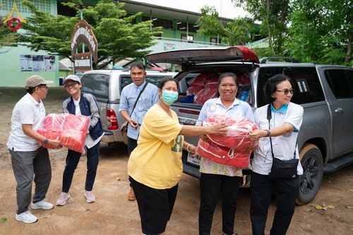 กลุ่มคนกำลังช่วยกันส่งมอบถุงยังชีพสีแดงจากท้ายรถกระบะให้กับผู้ประสบภัย