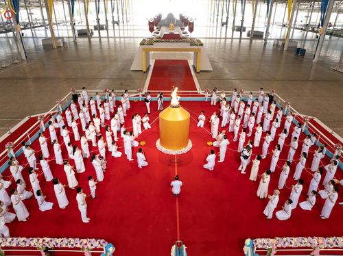 กลุ่มสาธุชนชุดขาวประกอบพิธีจุดเทียนใจ ไฟนิรันดร์ อนันตชัย บนพรมสีแดงภายในอาคาร