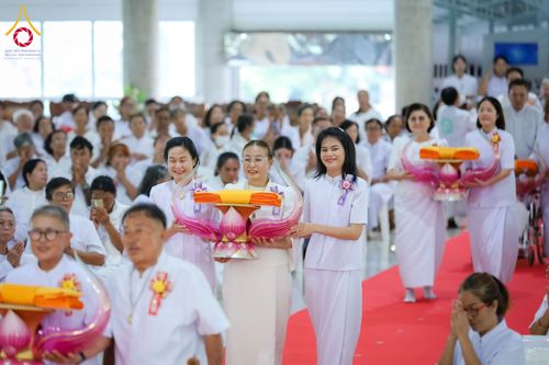 กลุ่มพุทธศาสนิกชนแต่งกายชุดสีขาวถือพานพุ่มผ้าไตรเดินแถวในอาคาร