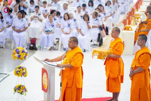 พระภิกษุสงฆ์กำลังกล่าวธรรมบรรยายที่โพเดียมในพิธีทางศาสนาที่มีสาธุชนชุดขาวนั่งร่วมงาน