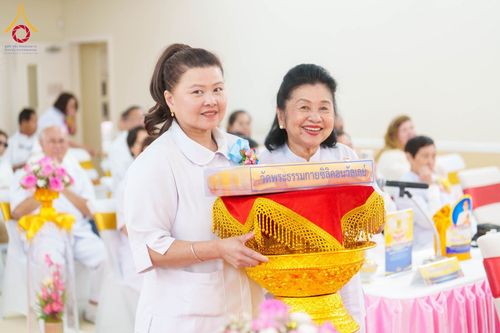 หญิงสองท่านสวมชุดสีขาวถือพานพุ่มผ้าไตรในพิธีทางศาสนา