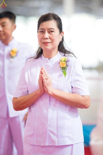 สุภาพสตรีสวมชุดสีขาวพนมมือและติดดอกไม้ที่หน้าอก