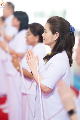 ผู้หญิงสวมชุดสีขาวกำลังพนมมือถือสายสิญจน์ในพิธีทางศาสนา