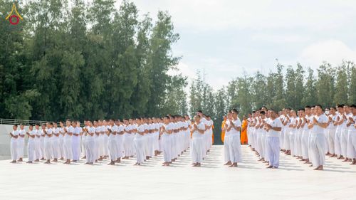กลุ่มนักเรียนนายสิบตำรวจสวมชุดขาวปฏิบัติธรรมยืนเรียงแถวพนมมือกลางแจ้ง