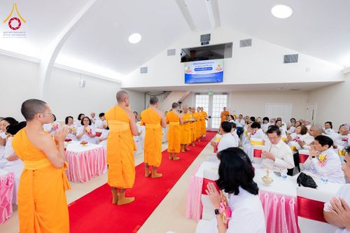 คณะสงฆ์กำลังประกอบพิธีทางศาสนาท่ามกลางพุทธศาสนิกชนที่นั่งพนมมือร่วมพิธีภายในอาคาร
