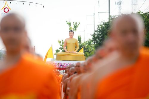 พระภิกษุสงฆ์จำนวนมากเดินนำหน้าพระพุทธรูปสีทองที่ประดิษฐานบนแท่นประดับดอกไม้ในพิธีทางศาสนา