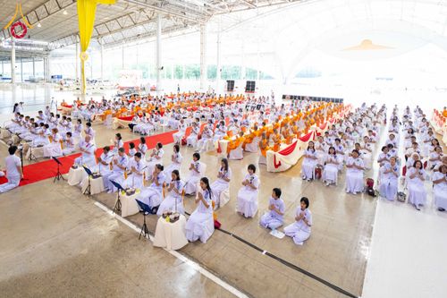 กลุ่มพุทธศาสนิกชนสวมชุดขาวนั่งพนมมือร่วมพิธีทางศาสนาภายในอาคารขนาดใหญ่