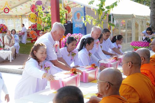 กลุ่มคนสวมชุดขาวกำลังถวายกล่องสังฆทานให้พระภิกษุสงฆ์ในงานพิธีทางศาสนา