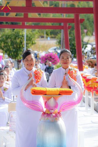 หญิงสองคนสวมชุดสีขาวพนมมือถือพานผ้าไตรในพิธีทางศาสนา