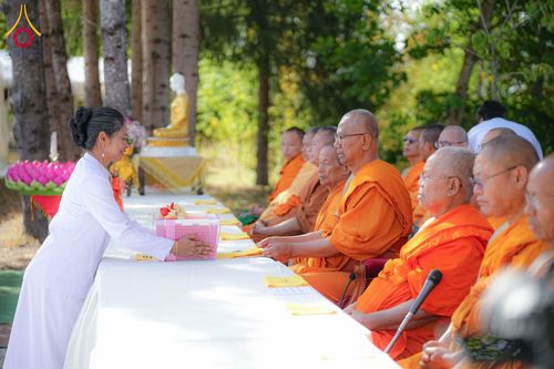 หญิงชุดขาวกำลังประเคนของถวายแด่พระภิกษุสงฆ์ในพิธีทางศาสนา