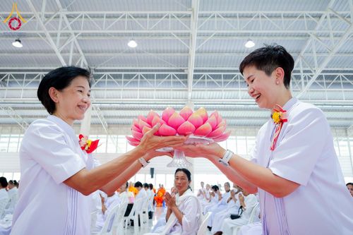 หญิงสองคนสวมชุดขาวกำลังประคองพานดอกบัวสีชมพูในพิธีทางศาสนา