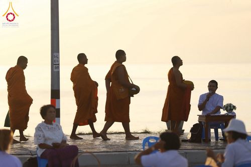 พระสงฆ์หลายรูปกำลังเดินรับบิณฑบาตริมชายหาดในช่วงเช้าท่ามกลางพุทธศาสนิกชน