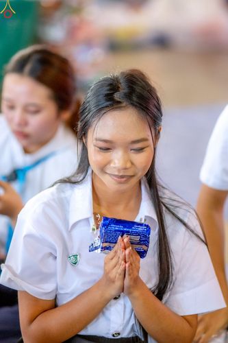 หญิงสาวสวมชุดนักศึกษาพนมมือถือห่ออาหารแห้งด้วยสีหน้าสงบ