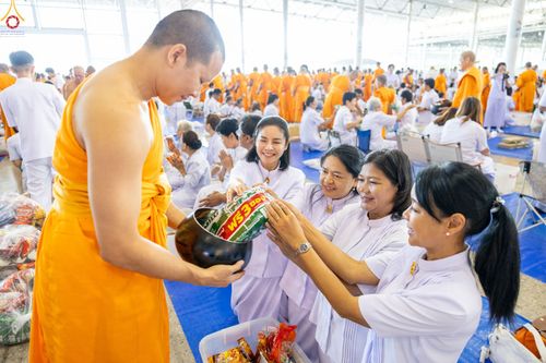 พุทธศาสนิกชนชุดขาวกำลังใส่บาตรข้าวสารอาหารแห้งแด่พระภิกษุสงฆ์ในพิธีตักบาตร