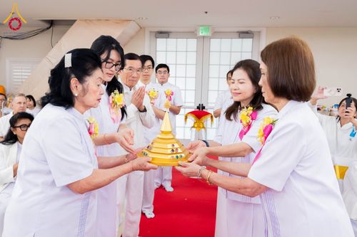 กลุ่มคนในชุดสีขาวกำลังถือพานสีทองที่มีเจดีย์จำลองบรรจุพระบรมสารีริกธาตุในพิธีทางศาสนา