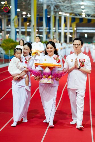 กลุ่มบุคคลในชุดสีขาวกำลังเดินถือพานพุ่มผ้าป่าบนพรมแดงภายในอาคาร