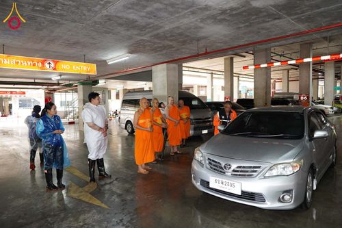 พระภิกษุสงฆ์และเจ้าหน้าที่ยืนรวมกลุ่มกันภายในอาคารจอดรถเพื่อตรวจดูความเรียบร้อย