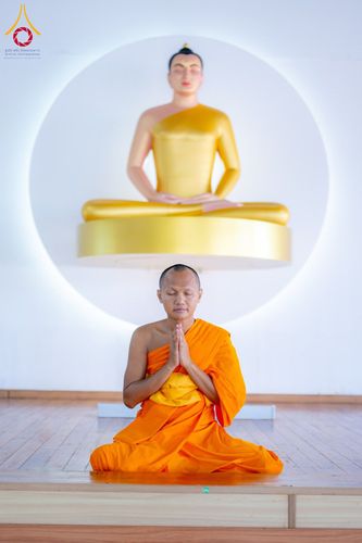พระภิกษุสงฆ์นั่งสมาธิพนมมืออยู่หน้าพระพุทธรูปสีทอง