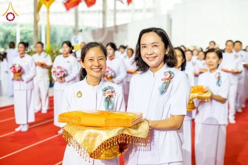 หญิงสองคนถือพานผ้าไตรจีวรในพิธีทางศาสนาท่ามกลางผู้เข้าร่วมงานที่สวมชุดสีขาว