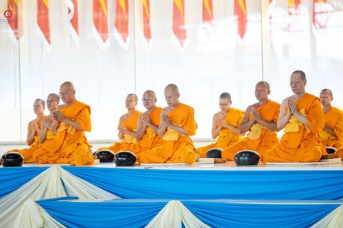 พระภิกษุสงฆ์หลายรูปนั่งเรียงแถวพนมมือบนเวทีในพิธีทางศาสนา