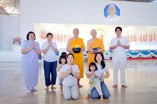 กลุ่มพุทธศาสนิกชนและพระภิกษุสงฆ์ยืนและนั่งพนมมือร่วมกันภายในอาคารสภาธรรมกายสากล