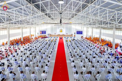 พุทธศาสนิกชนจำนวนมากสวมชุดขาวนั่งบนเก้าอี้ภายในอาคารโถงกว้างเพื่อร่วมพิธีทางศาสนา
