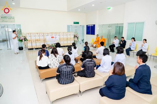 กลุ่มบุคคลและพระภิกษุสงฆ์นั่งร่วมในพิธีมอบยาและเวชภัณฑ์ภายในอาคารบุญรักษา