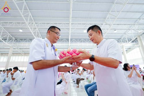 ชายสองคนสวมชุดสีขาวกำลังถือพานดอกบัวสีชมพูร่วมกันในพิธีทางศาสนา