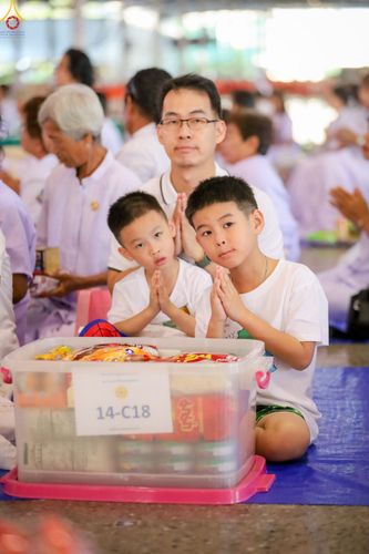 ชายและเด็กชายสองคนพนมมือไหว้หน้ากล่องใส่ของตักบาตรในพิธีทำบุญ