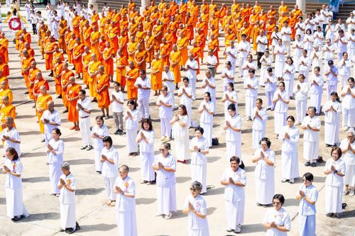 พระภิกษุสงฆ์และพุทธศาสนิกชนชุดขาวจำนวนมากยืนเข้าแถวร่วมพิธีทางศาสนา
