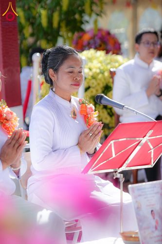 หญิงสาวสวมชุดสีขาวพนมมือไหว้หน้าไมโครโฟนในพิธีกรรมทางศาสนา