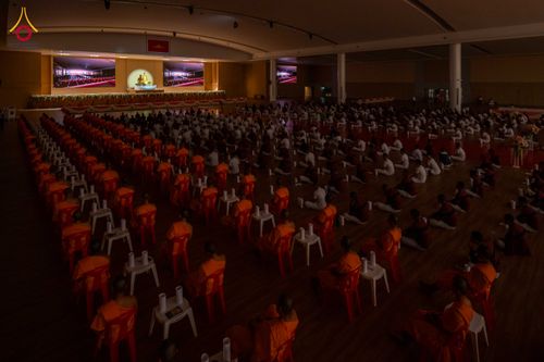 ผู้เข้าร่วมโครงการในชุดสีขาวและพระภิกษุนั่งปฏิบัติธรรมพร้อมเทียนในโถงกว้าง