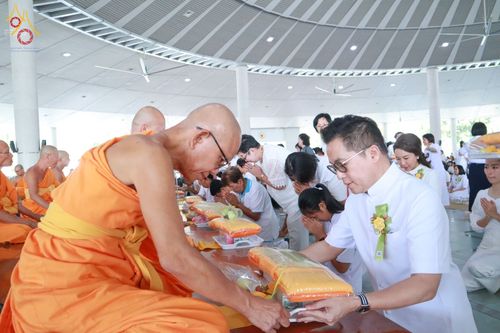 พุทธศาสนิกชนชายสวมชุดขาวกำลังประเคนไทยธรรมแด่พระภิกษุสงฆ์ในพิธีบุพเปตพลี ณ หอฉันคุณยายอาจารย์มหารัตนอุบาสิกาจันทร์ ขนนกยูง วัดพระธรรมกาย