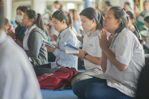 กลุ่มเยาวชนหญิงนั่งพนมมือและถือหนังสือสวดมนต์ร่วมกิจกรรมสวดธัมมจักกัปปวัตตนสูตร