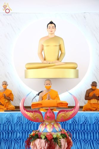 พระสงฆ์สามรูปนั่งประกอบพิธีทางศาสนาเบื้องหน้าพระพุทธรูปปางสมาธิสีทอง