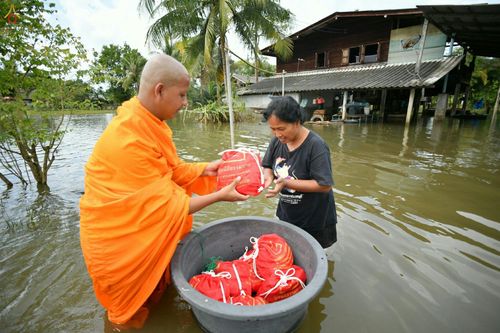 พระสงฆ์กำลังส่งมอบถุงยังชีพสีแดงให้แก่หญิงชาวบ้านในพื้นที่น้ำท่วมขัง
