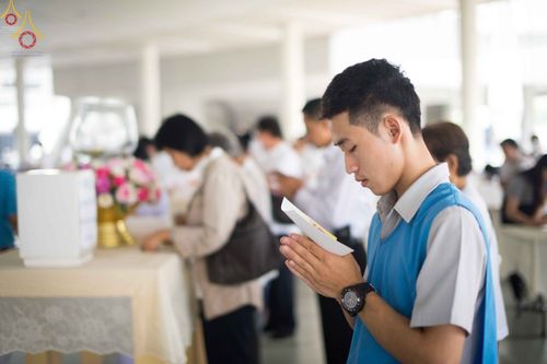 ชายหนุ่มพนมมือถือซองปัจจัยด้วยความสำรวมในพิธีปุพพเปตพลี ณ วัดพระธรรมกาย