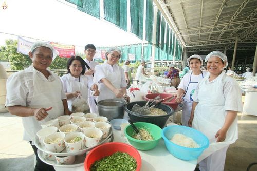 กลุ่มอาสาสมัครสวมชุดขาวกำลังช่วยกันจัดเตรียมอาหารใส่ถ้วยในโรงทาน